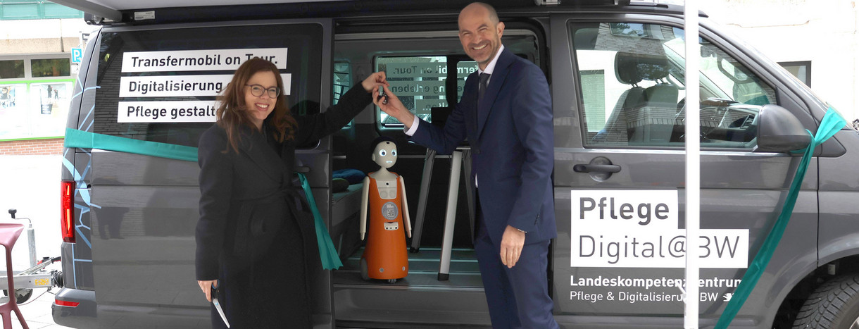 Ministerialdirektorin Leonie Dirks steht vor Transfermobil und übergibt Fahrzeugschlüssel an Prof. Dr. Daniel Buhr vom Landeskompetenzzentrum Pflege & Digitalisierung.